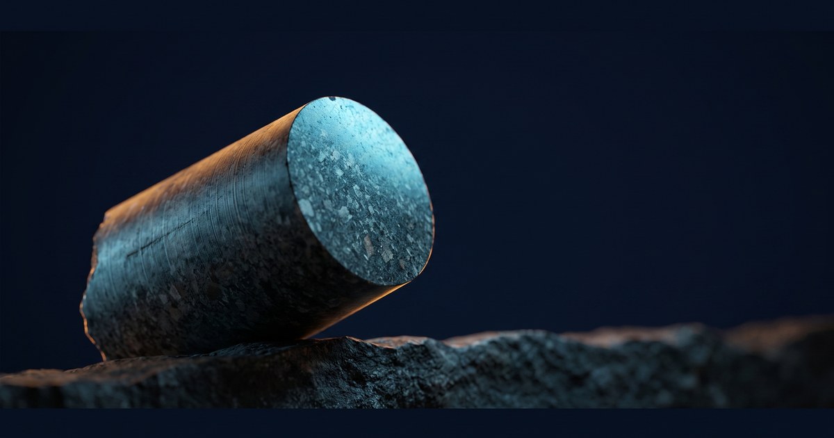 A single cylindrical rock core resting at an angle on dark stone, cyan light raking its cut face and amber along one edge