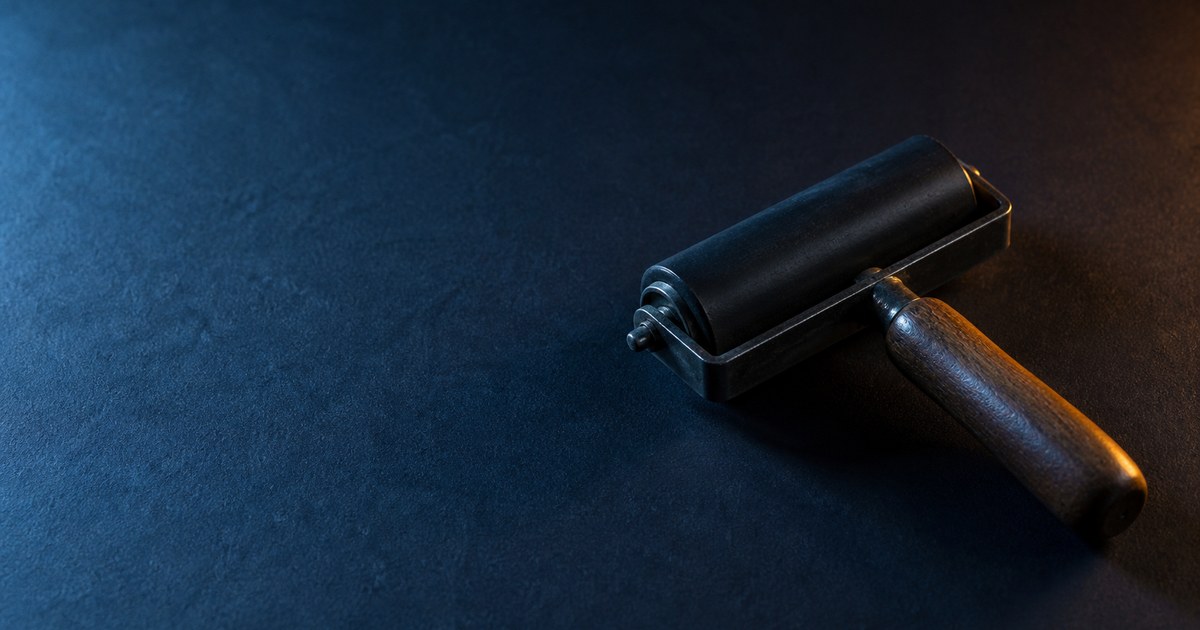 A vintage printing ink brayer resting on dark textured paper under cyan and amber directional light